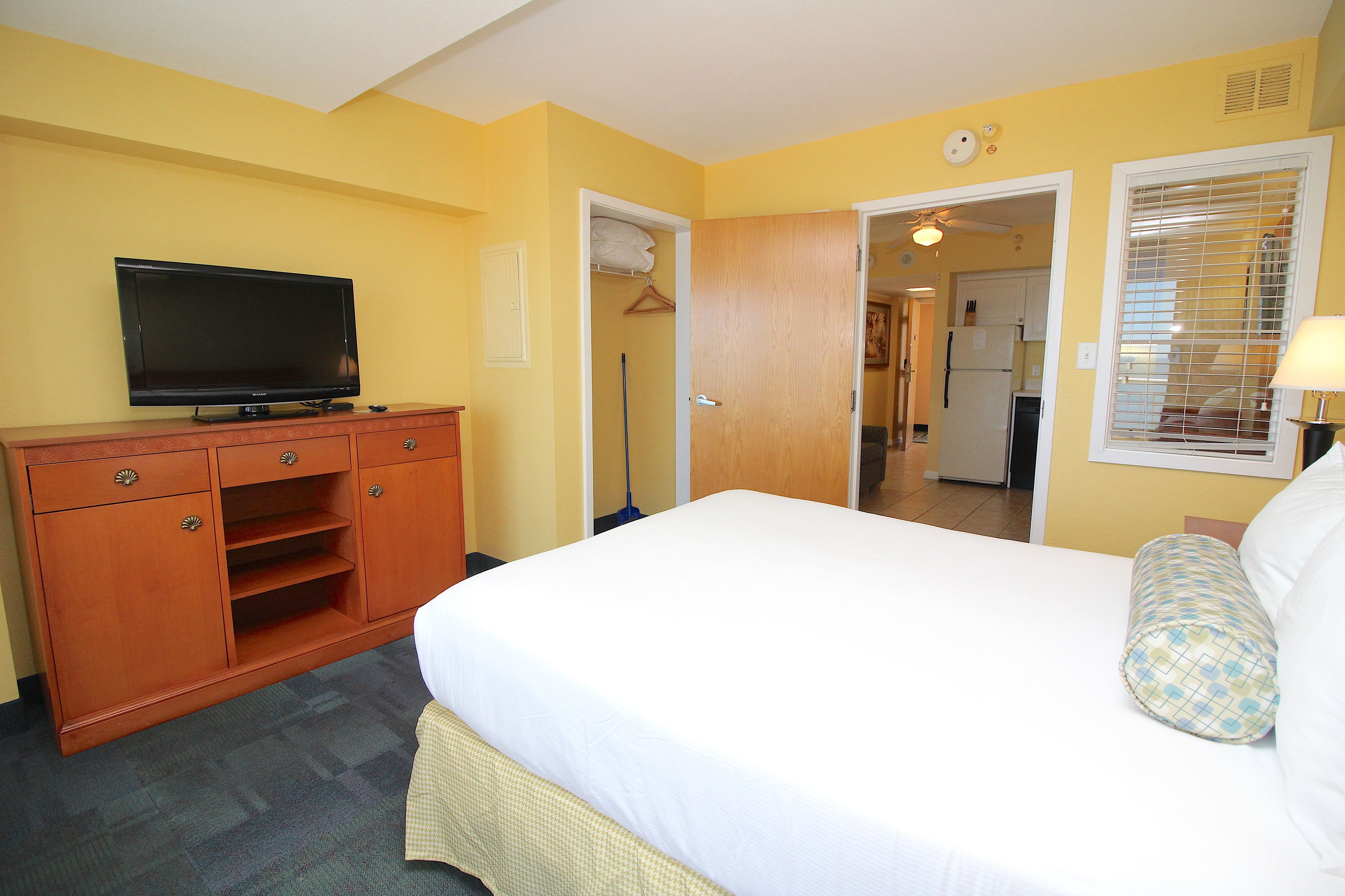 A hotel room with a bed, a television on a wooden dresser, a closet, and a bathroom visible through an open door.