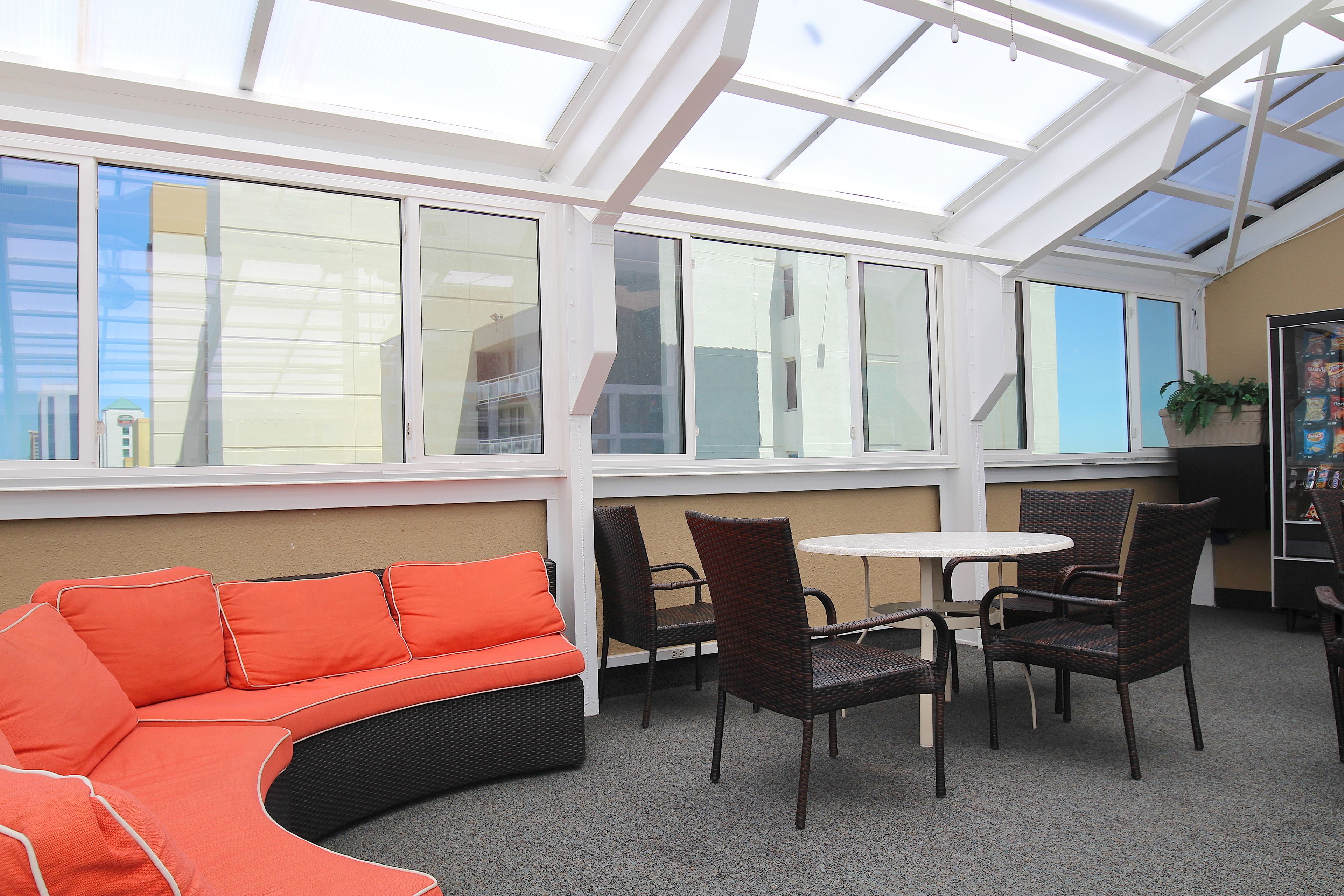 A sunlit patio area with a curved orange sofa, wicker chairs, and a small round table.