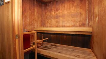 Una sauna in legno con panche e ripiano contenente un catino e un cucchiaio di legno.