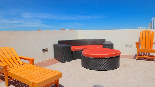 An outdoor seating area with wicker furniture and orange Adirondack chairs. - Ocean Sands Resort, Oceanfront, Virginia Beach by Vacatia (Virginia Beach)