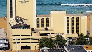 A building with a sign reading "Ocean Sands Resort" near a beach. - Ocean Sands Resort, Oceanfront, Virginia Beach by Vacatia (Virginia Beach)