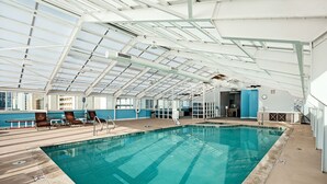An indoor swimming pool with clear glass ceilings, lounge chairs, and a view of the city. - Ocean Sands Resort, Oceanfront, Virginia Beach by Vacatia (Virginia Beach)
