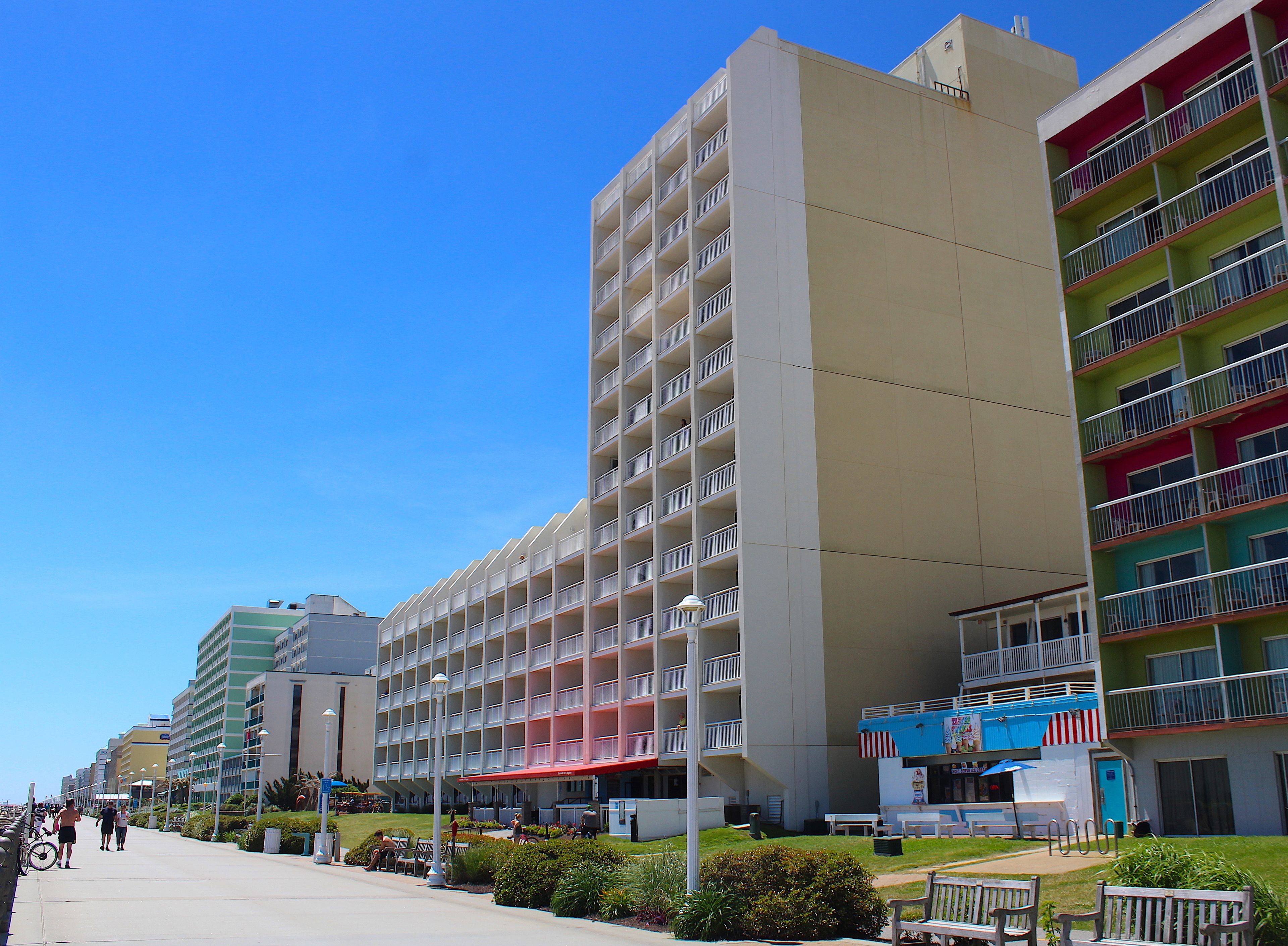 Un hôtel à plusieurs étages, doté de balcons, d’un espace extérieur aménagé et abrité, et surplombant un ciel d’un bleu éclatant.