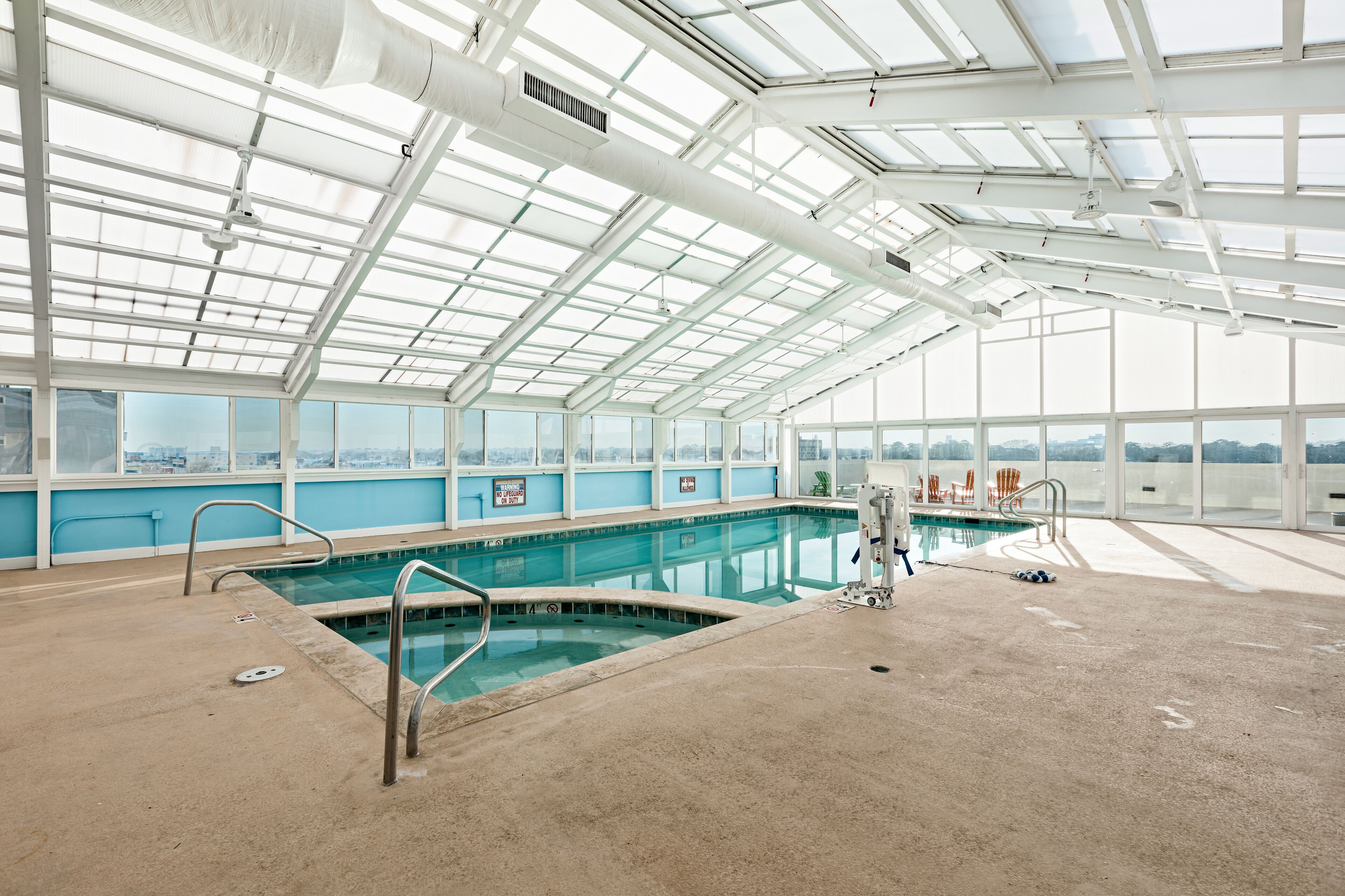 An indoor swimming pool with a glass ceiling, clear view of the city, and a lifeguard chair.