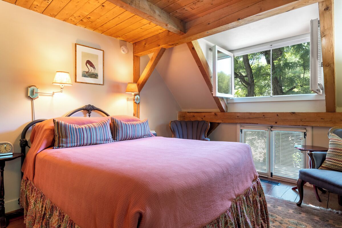 A bedroom with a large bed, a wooden ceiling, a window with blinds, and a chair.