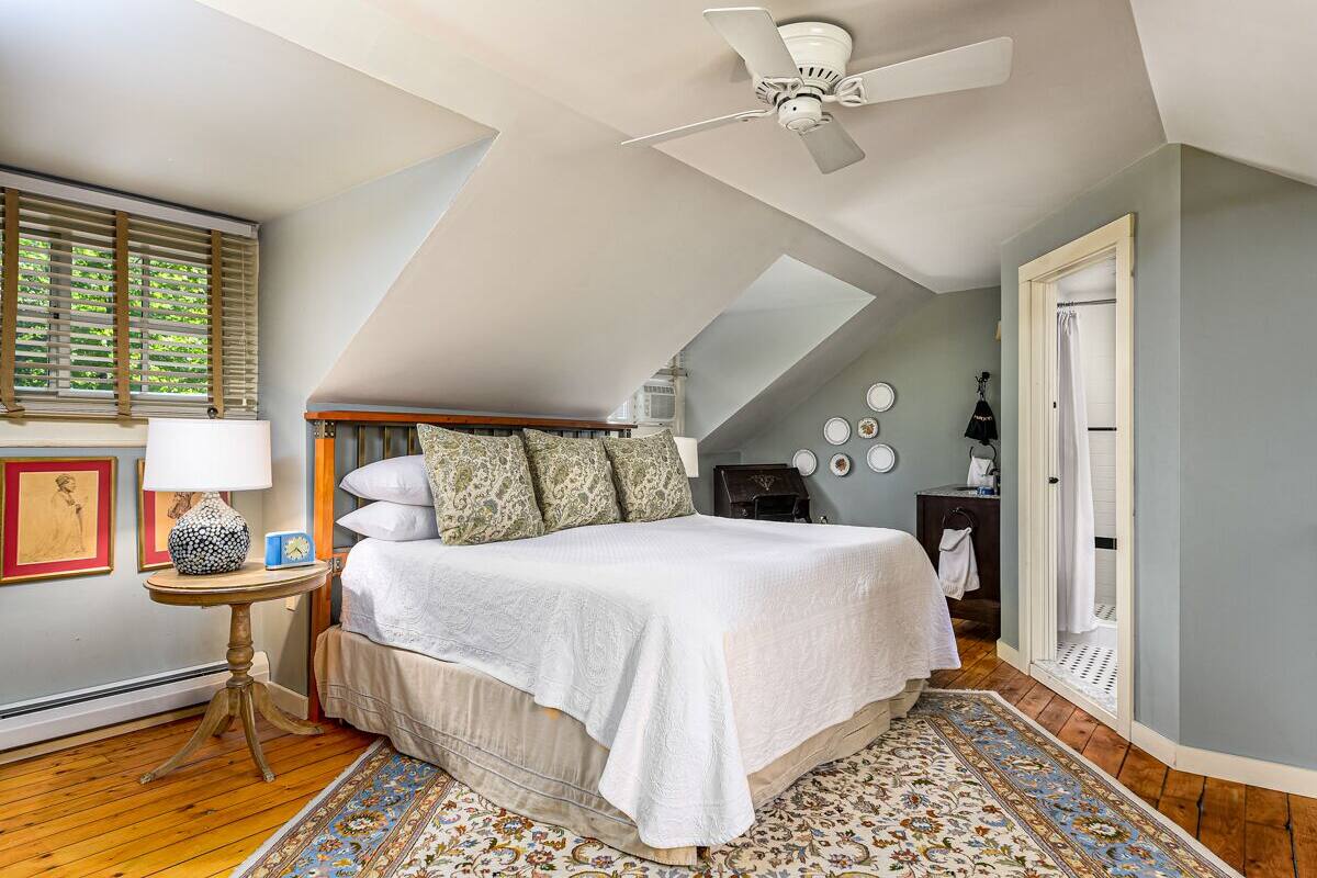 A bedroom with a bed, a ceiling fan, a window with blinds, a bedside table, and a rug.