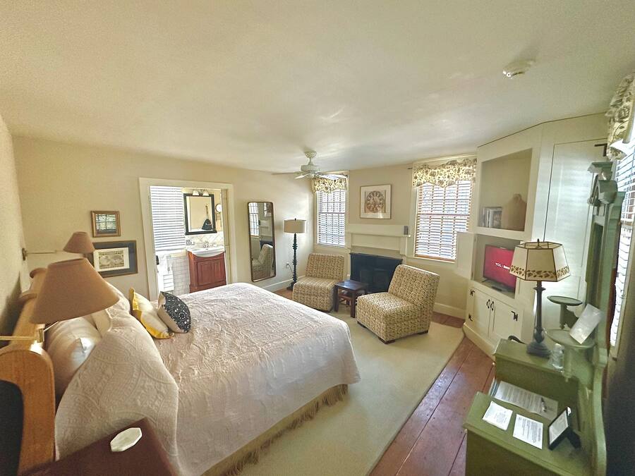 A bedroom with a large bed, two chairs, a desk, and a vanity with a mirror.