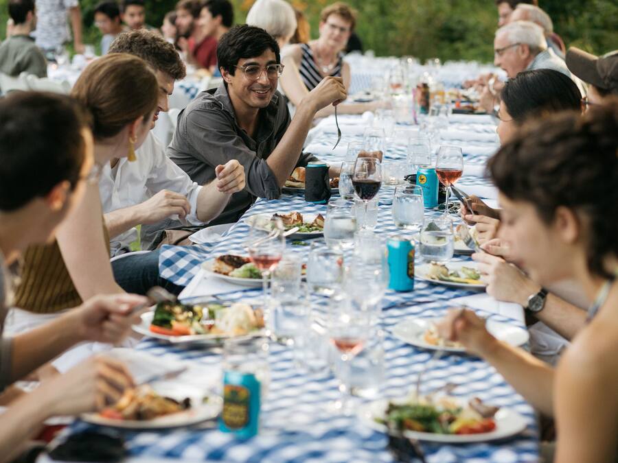 Un grupo de personas cenando en una mesa al aire libre con mantel a cuadros.