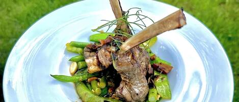 A white bowl with a handle containing a dish of meat and green vegetables.