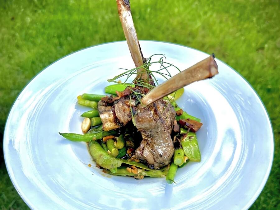 A white bowl with a handle containing a dish of meat and green vegetables.