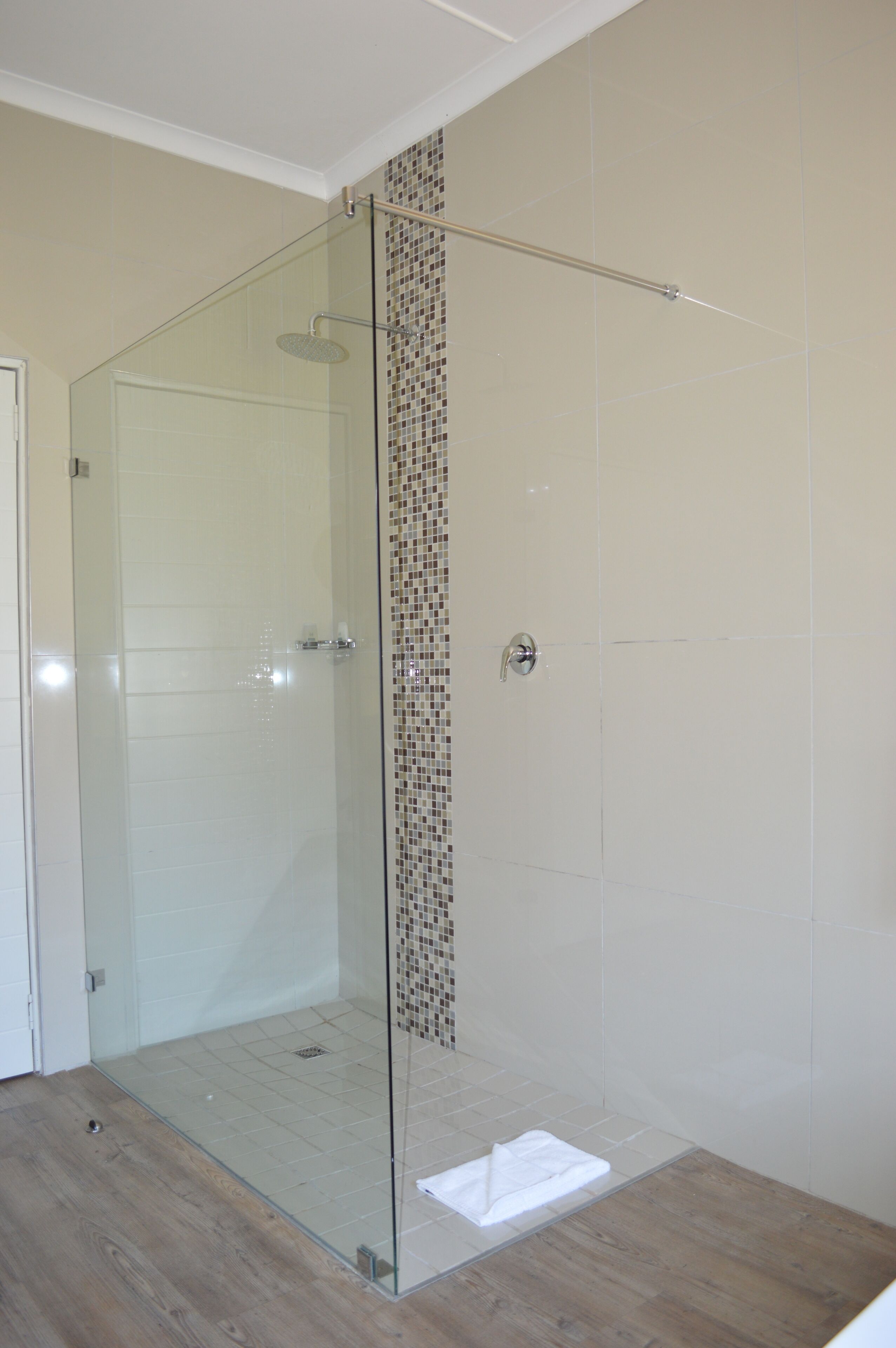 A glass-enclosed shower with a tiled wall and a wooden floor.
