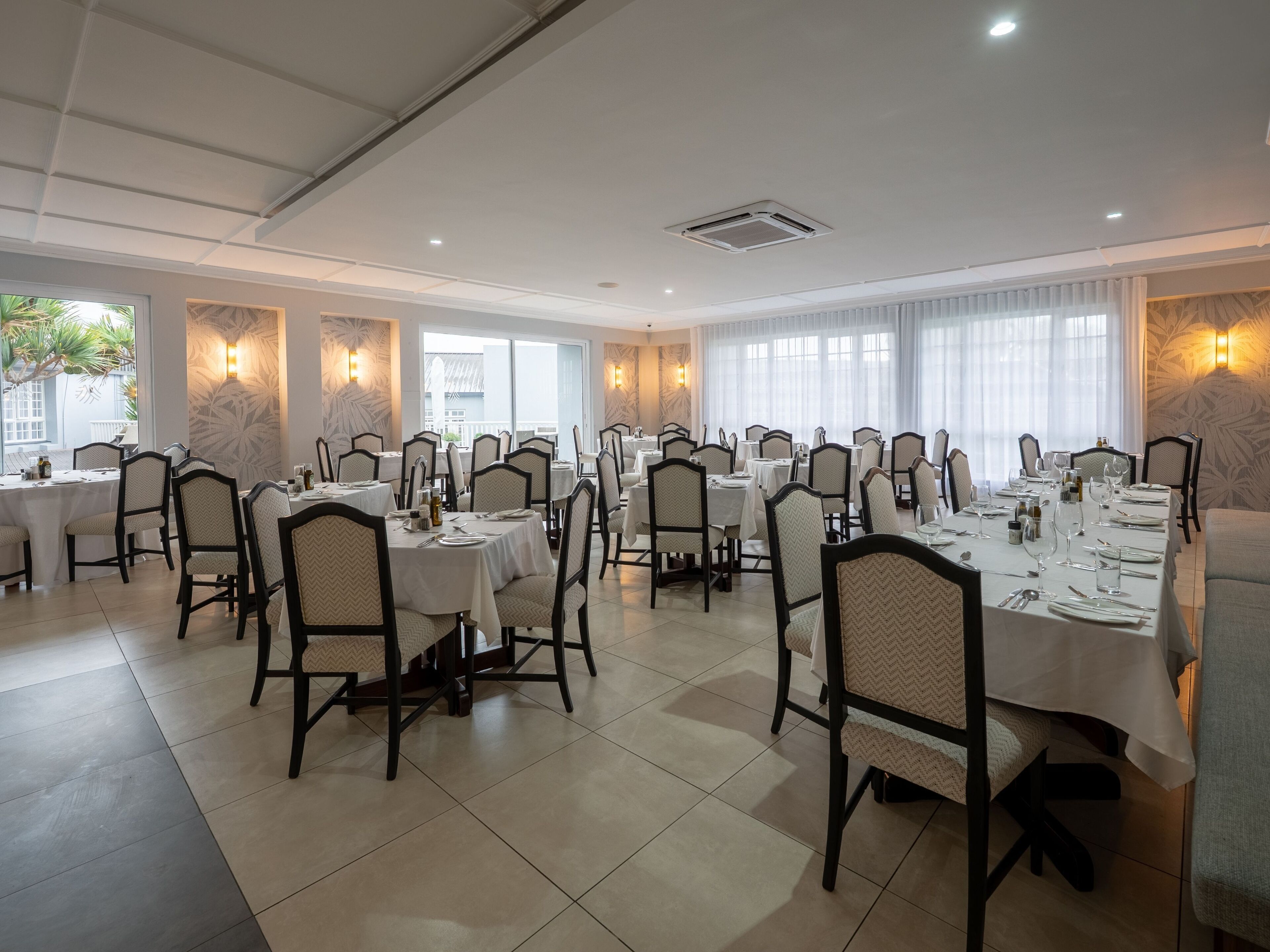 Un comedor con varias mesas y sillas dispuestas en filas, con ventilador de techo e iluminación empotrada.