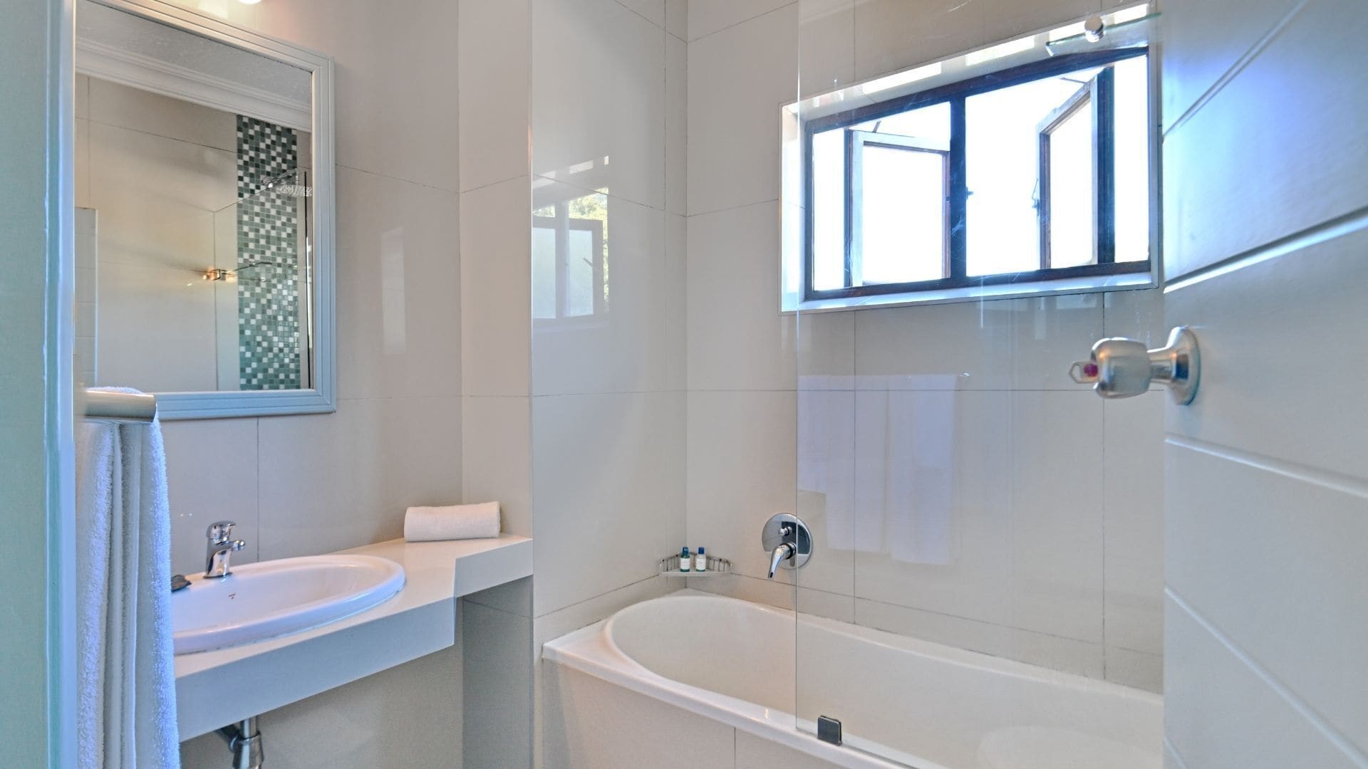 A modern bathroom with a white sink, a bathtub, and a window above the bathtub.
