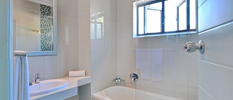 A modern bathroom with a white sink, a bathtub, and a window above the bathtub.