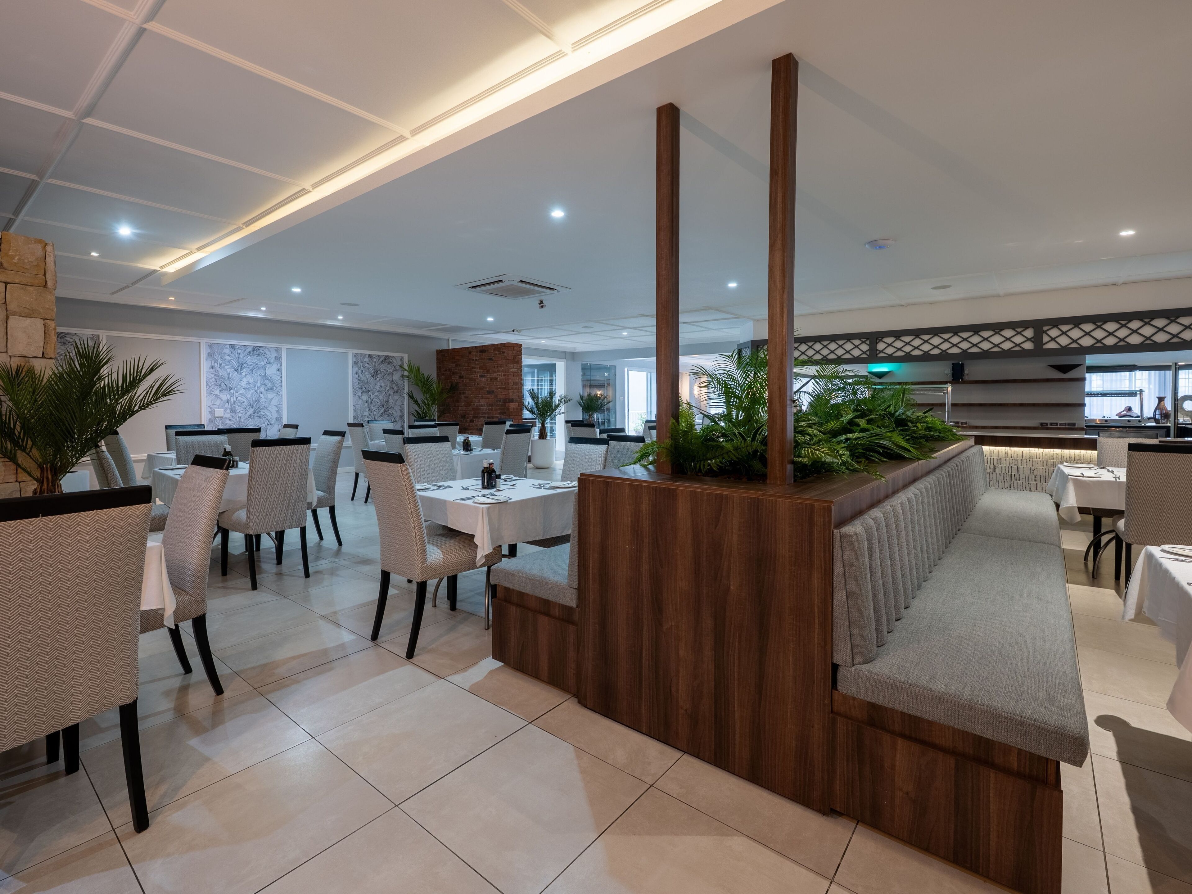 Un espace de restauration moderne, doté de plusieurs tables et chaises, d’un comptoir d’accueil en bois et de plantes en pot.