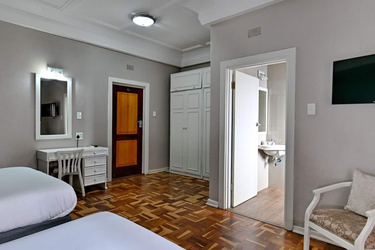 Une chambre d’hôtel comprenant un lit, un bureau avec une chaise, une armoire, une salle de bain avec un lavabo et un téléviseur.