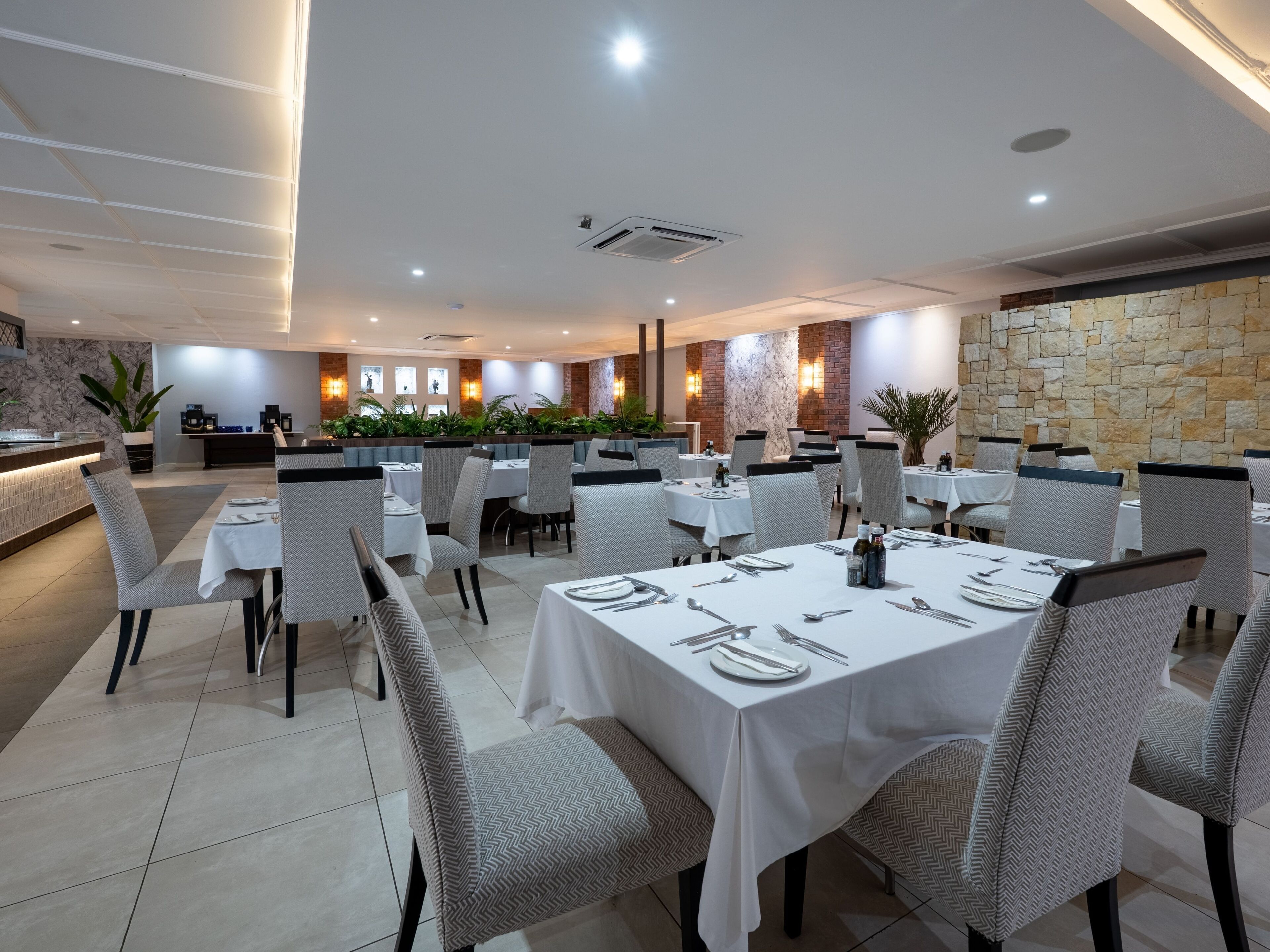 A modern dining area with white tablecloths, grey patterned chairs, and a stone accent wall.