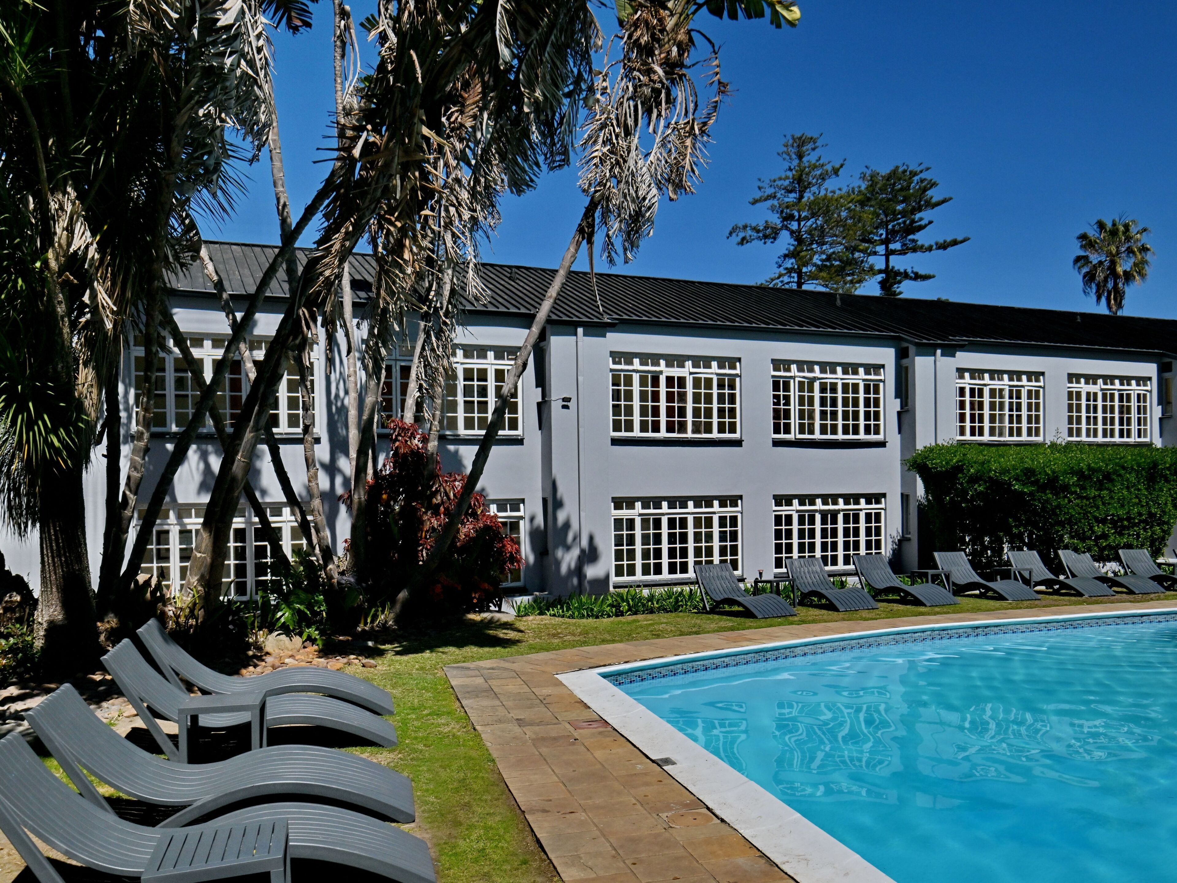 Zona junto a la piscina con sillones reclinables, una piscina y un edificio de techos planos y amplias ventanas.