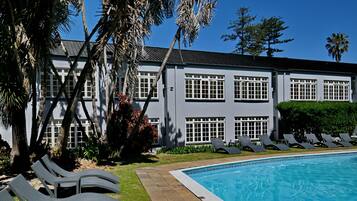 Zona junto a la piscina con sillones reclinables, una piscina y un edificio de techos planos y amplias ventanas.
