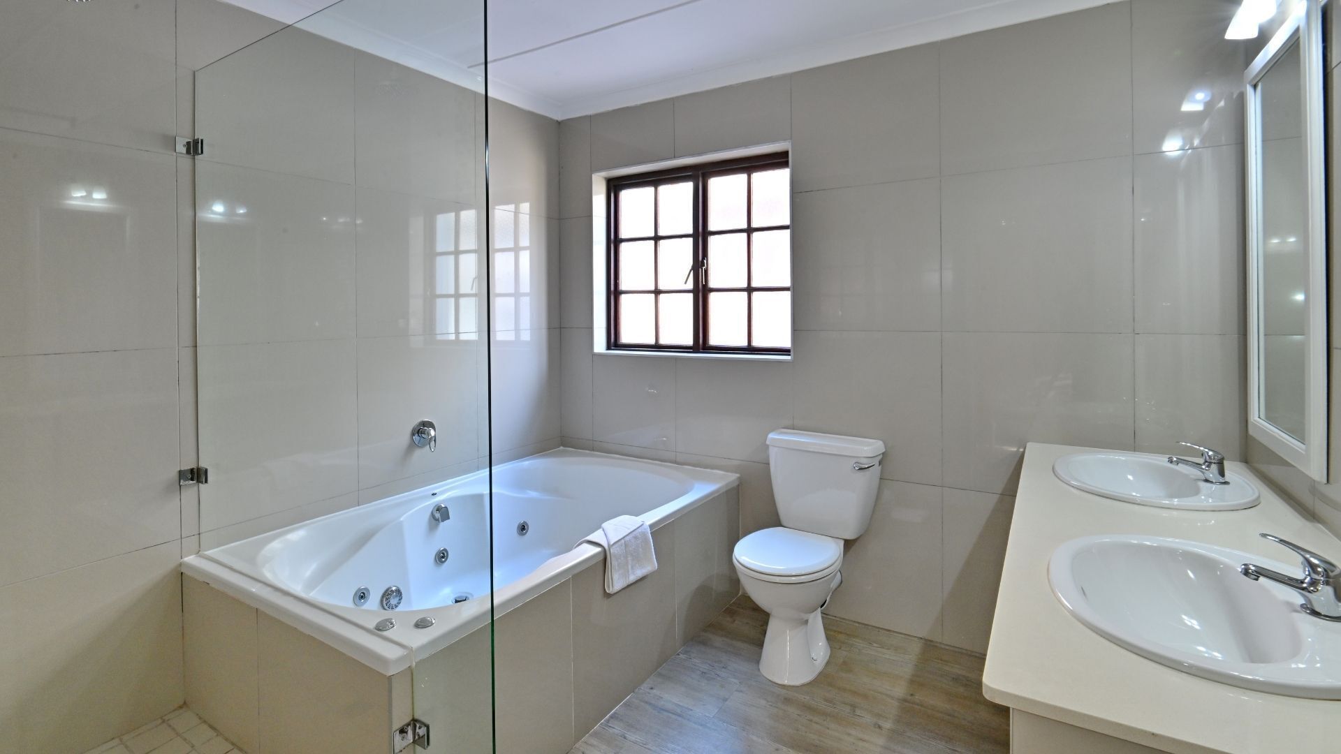 Un baño moderno con ducha de vidrio, bañera, inodoro y tocador con lavamanos.