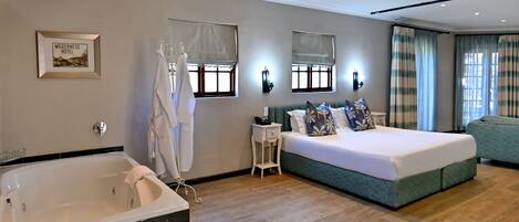 A modern bedroom with a large bed, a separate sitting area, a bathtub, and a window with curtains.