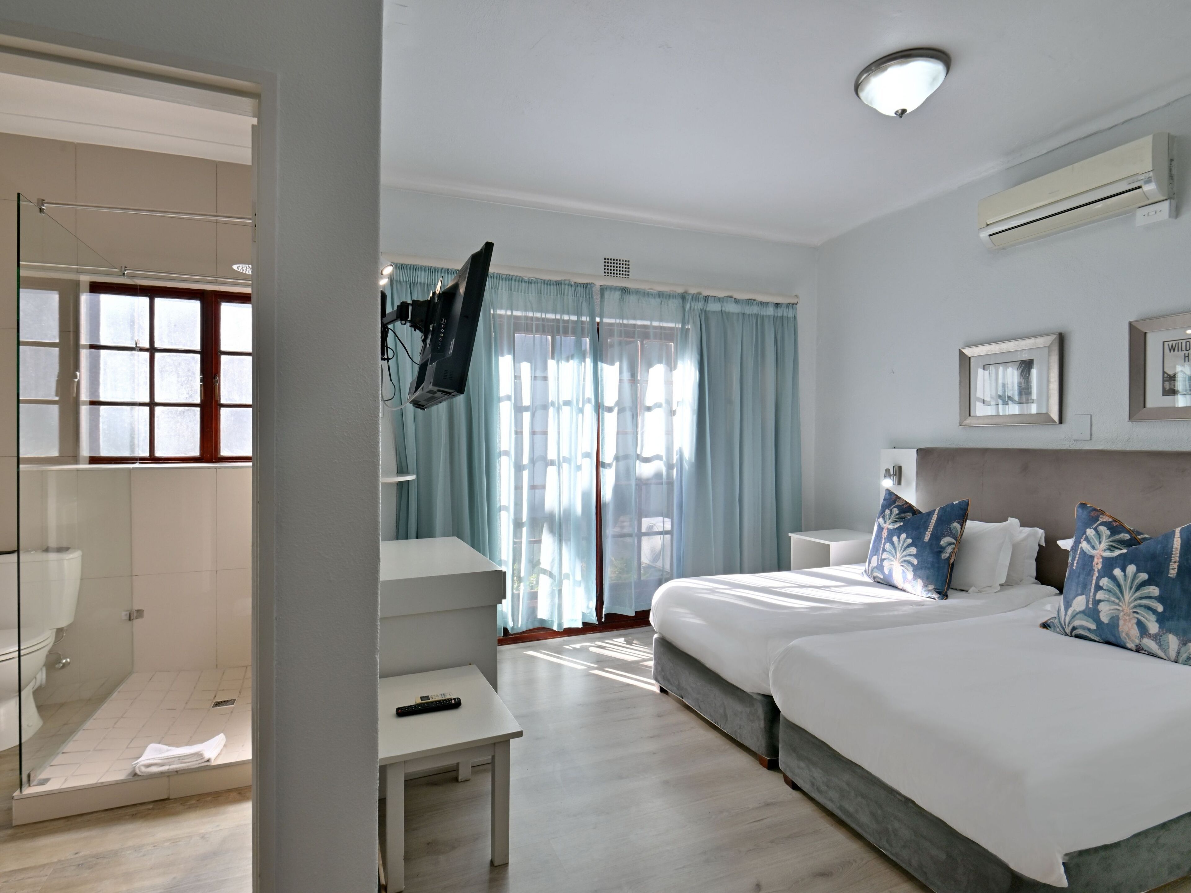 A hotel room with a bed, bedside tables, a TV, and a window with curtains.