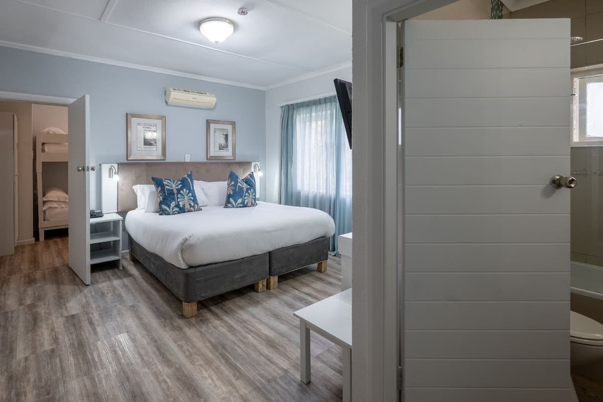 Une chambre à coucher avec un lit, des tables de chevet, une armoire et une salle de bain visible à travers une porte ouverte.