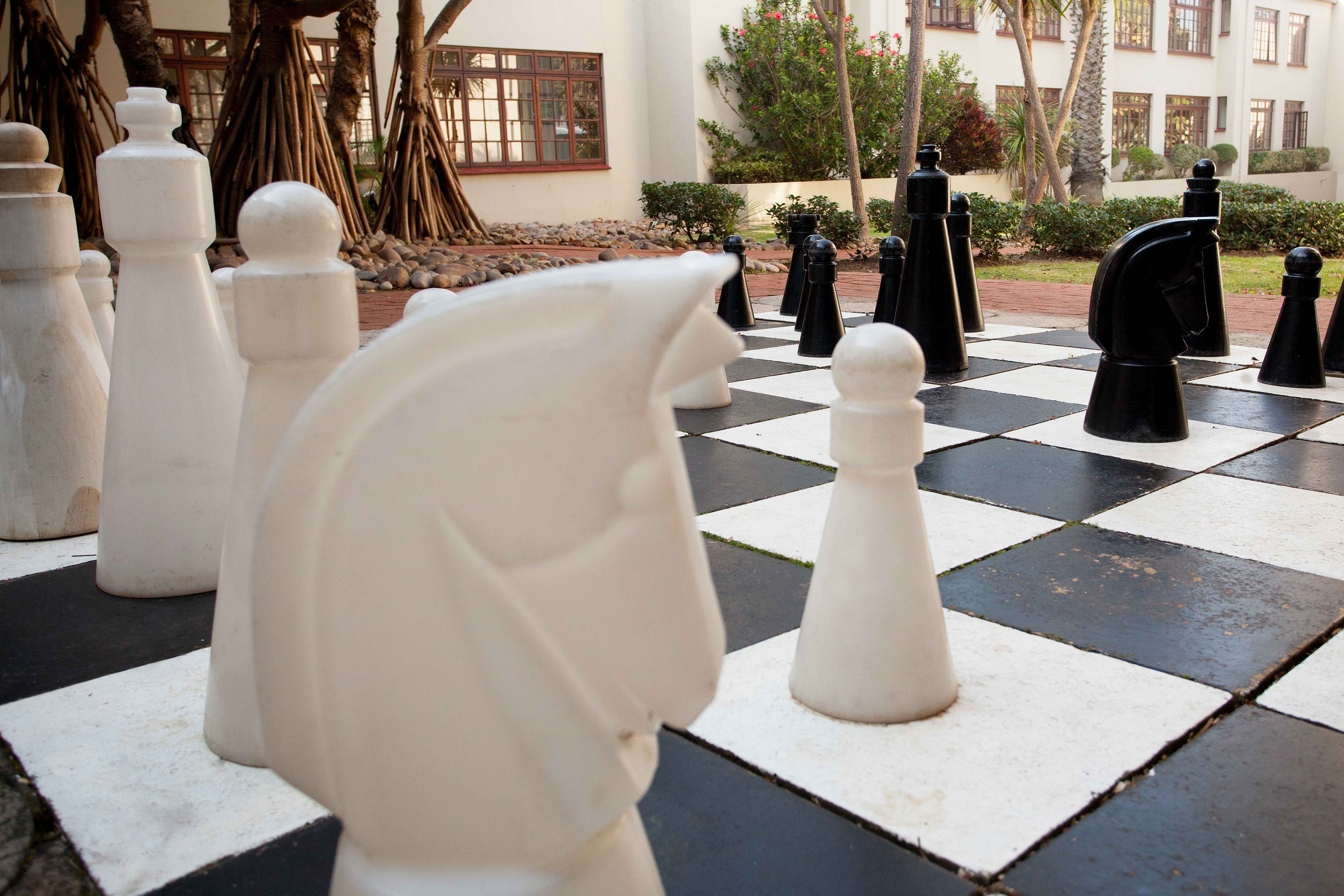 A chessboard with white and black pieces in an outdoor setting.