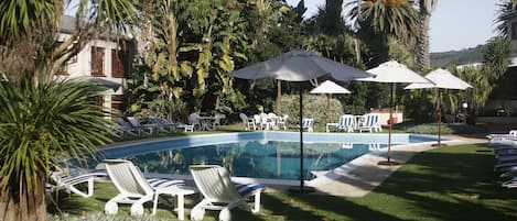 Una piscina al aire libre, sombrillas, sillones reclinables de piscina