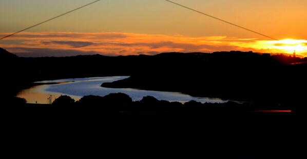 Un atardecer sobre un río, con la silueta de colinas al fondo.