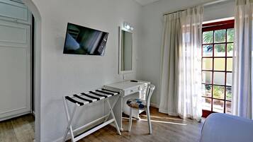 A room with a white desk, a mirror, a TV mounted on the wall, and a window with curtains.