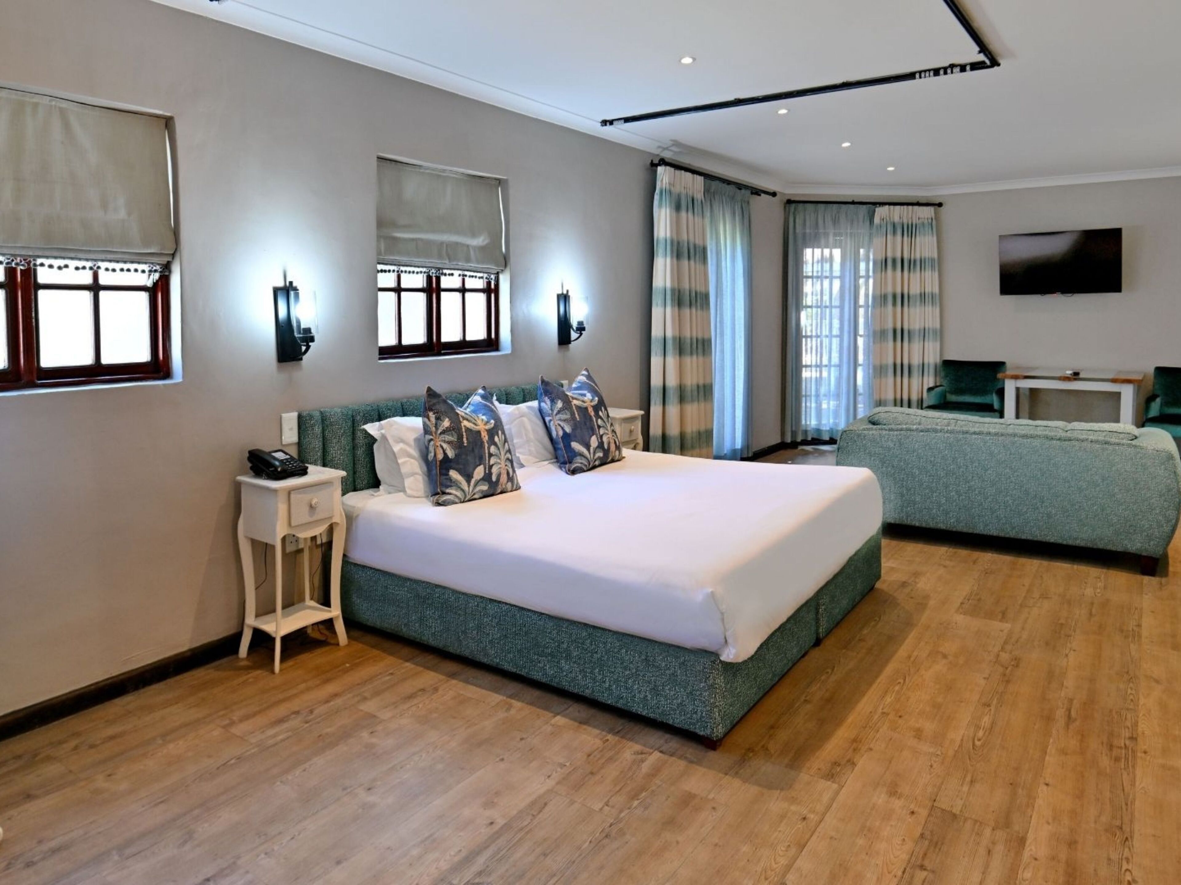 Una habitación de hotel moderna con una cama grande, un sofá más pequeño, un televisor y un escritorio con un teléfono.