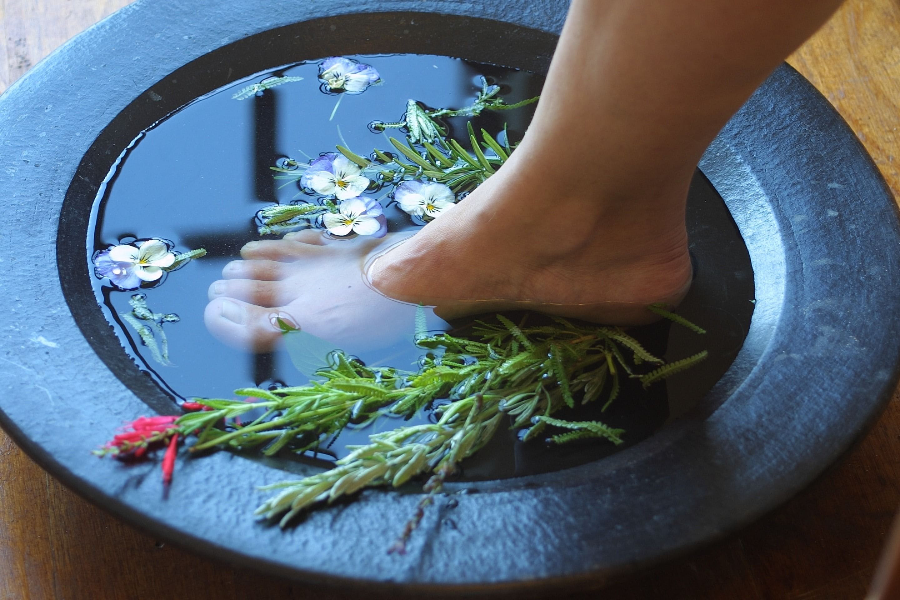A foot in a stone basin with water, flowers, and greenery.