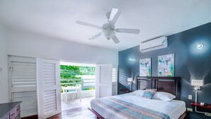 A bedroom with a bed, a ceiling fan, an air conditioning unit, and a view of greenery outside. - Negril Beach Club (Negril)