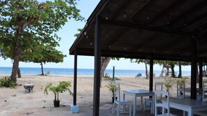 An outdoor seating area with tables and chairs, a covered section, and a view of the beach and ocean. - Negril Beach Club (Negril)