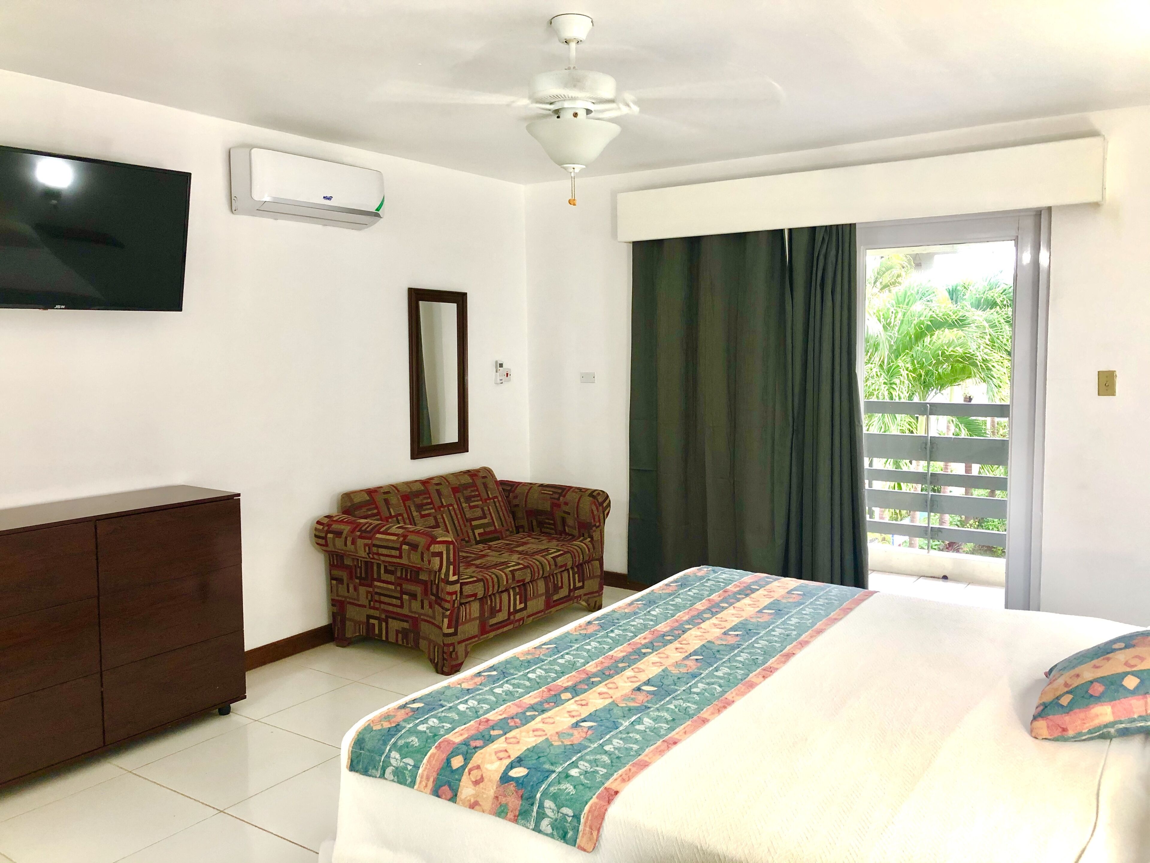 A hotel room with a bed, a sofa, a TV, an air conditioner, and a window with curtains.