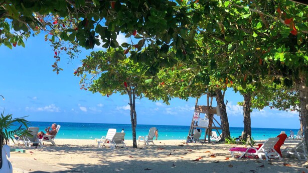 A beach with white lounge chairs, a wooden structure, and a clear blue sky. - Negril Beach Club (Negril)