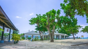 A building with a blue and white facade, a covered outdoor area, and several trees. - Negril Beach Club (Negril)