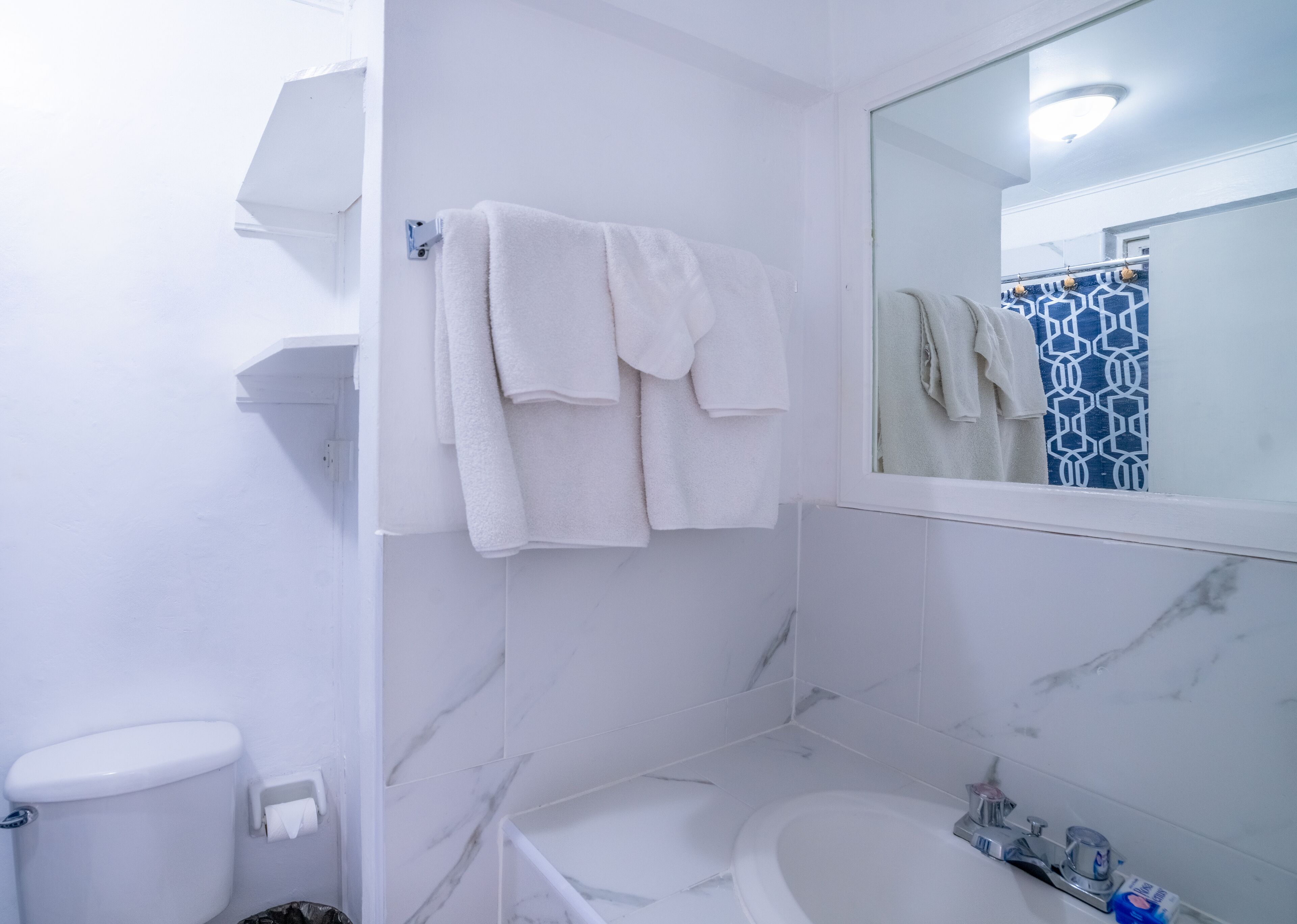 Un baño con inodoro, lavamanos y bañera. Toallas blancas cuelgan de un perchero.