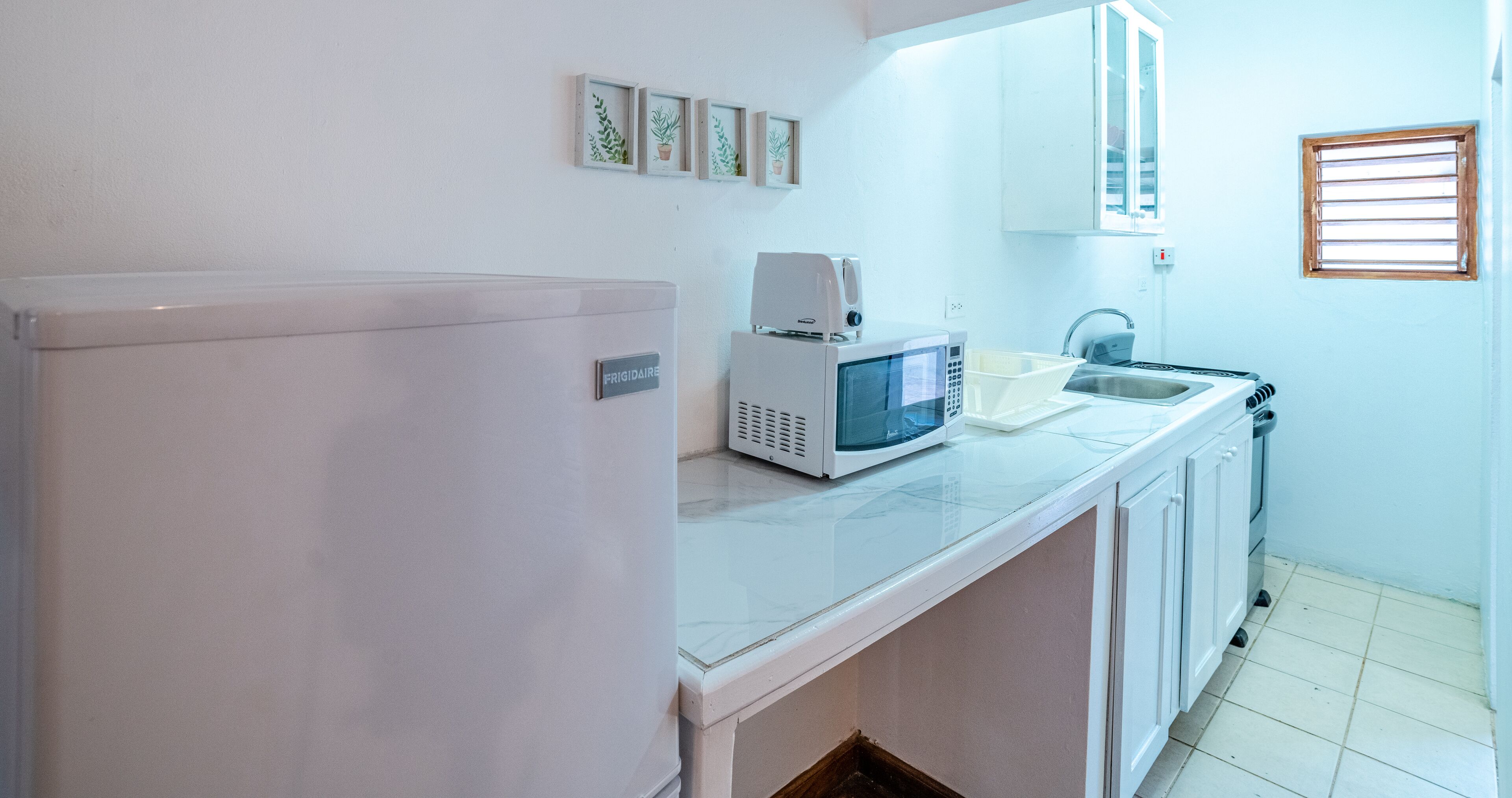 A kitchen with a white refrigerator, a microwave, a sink, and a window with blinds.