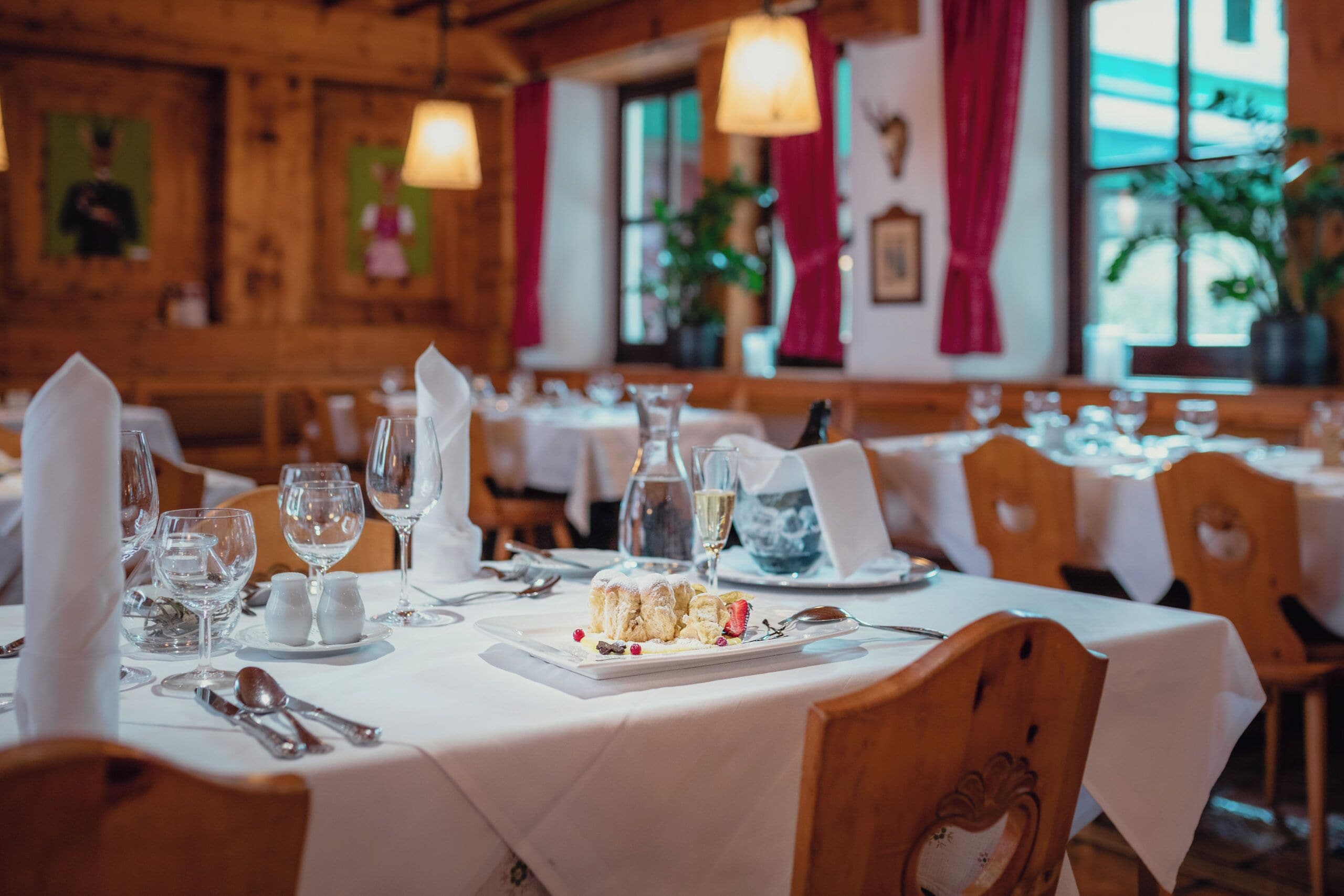 A restaurant interior with wooden walls, white tablecloths, and neatly set dining tables.