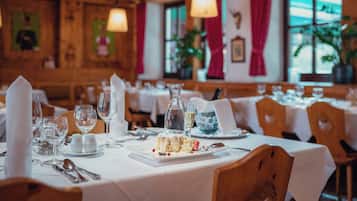 A restaurant interior with wooden walls, white tablecloths, and neatly set dining tables.