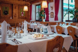 A restaurant interior with wooden walls, white tablecloths, and neatly set dining tables.