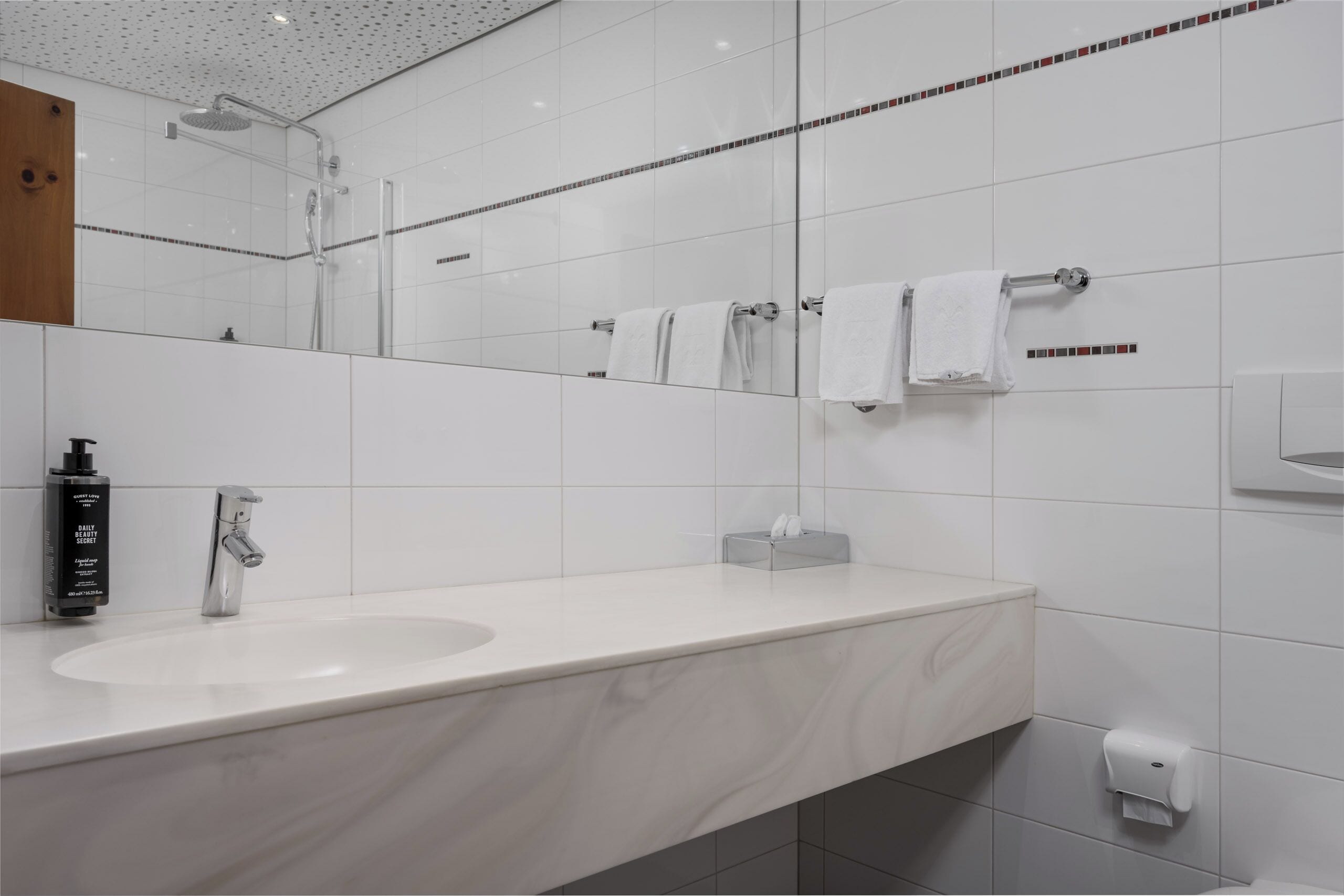 Een moderne badkamer met een marmeren wastafel, een handdouche en een grote spiegel.