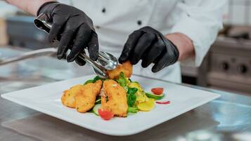 Un chef con uniforme blanco y guantes negros preparando comida en un plato blanco.