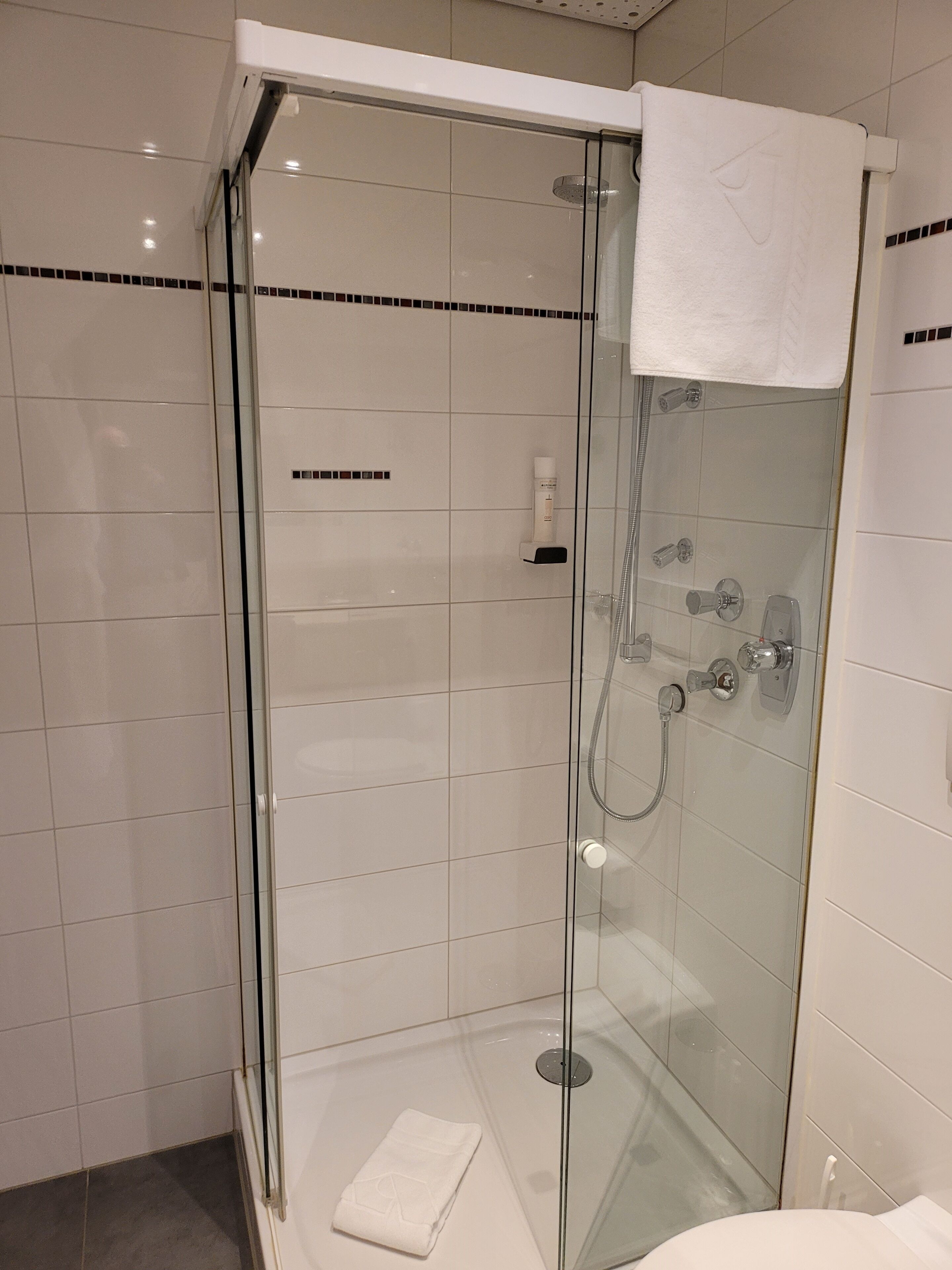 Une douche fermée par des parois de verre, avec une serviette blanche accrochée à la porte.