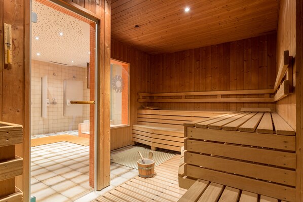 A wooden sauna with benches and a small bucket.