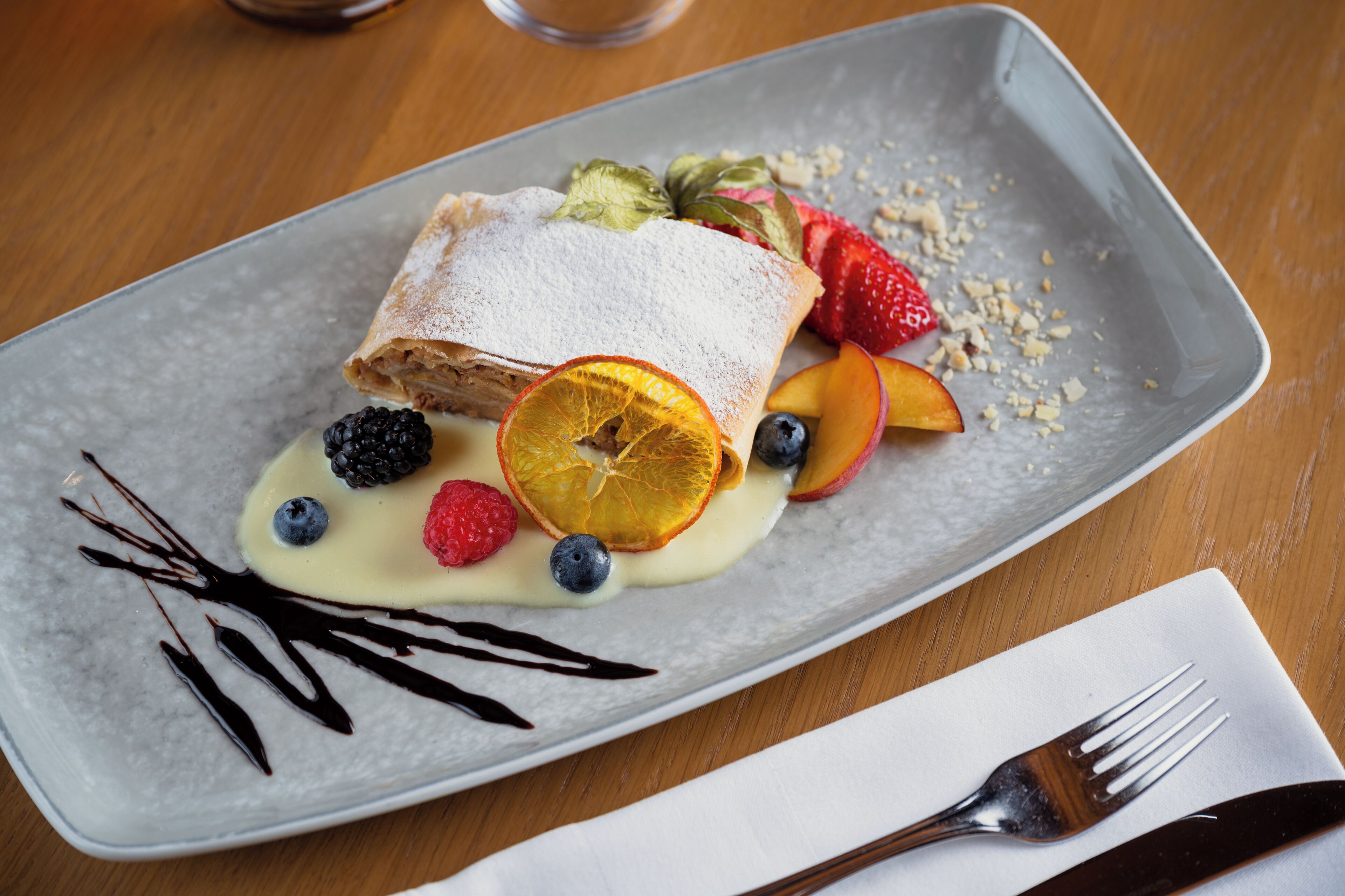 A dessert plate with a pastry, fruit, and chocolate drizzle.