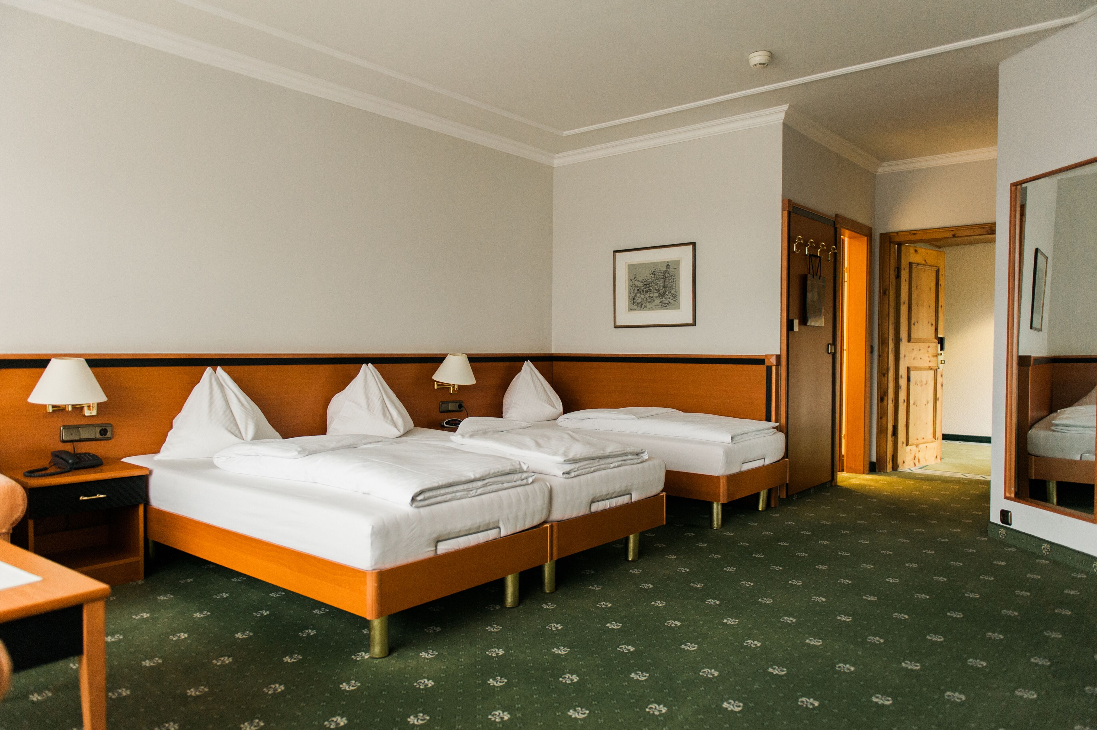 A hotel room with two single beds, a desk with a lamp, a telephone, and a framed picture on the wall.