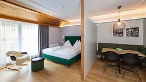 Moderni hotellihuone, jossa on puinen katto, vihreä sohva, valkoisilla vuodevaatteilla varustettu sänky ja ruokailutila, jossa on mustat tuolit.